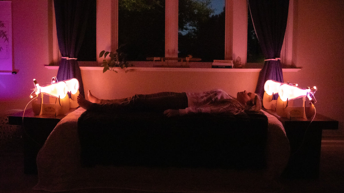 dimly lit room with a woman laying on a bed between the Theraphi bulbs